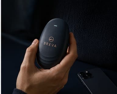 A hand holding BREVA while a phone lies face-down, out of focus, in the background
